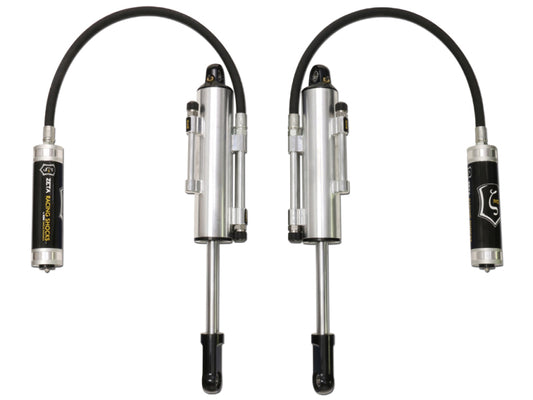 The image displays a pair of ICON 10-14 Ford Raptor Front Secondary 3.0 Zeta Series Shocks RR, showcasing silver, cylindrical automotive shock absorbers equipped with black flexible hoses. These shocks feature easy-to-adjust knobs and prominently display the ICON logo on their branded labels. They are positioned parallel against a plain white background, evoking the design elements of components used in the Ford SVT Raptor series.
