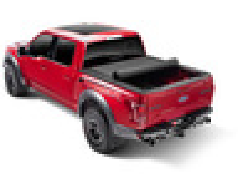 A red, modern pickup truck viewed from a rear angle showcases a sleek design with large tires and features the BAK brand's 16-20 Toyota Tacoma Revolver X4s 6.2ft Bed Cover roll-up hard cover, set against a plain white background.