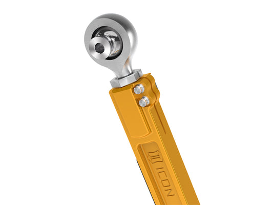 A detailed view of a metallic yellow rear lower link from ICON, designed for the 22-23 Toyota Tundra and 2024 Toyota Tacoma. This component is crafted from CNC machined 6061 aluminum with a gold anodized finish, and features a spherical PTFE-lined FK rod end for automotive applications. Embossed details are present, along with two visible bolts.