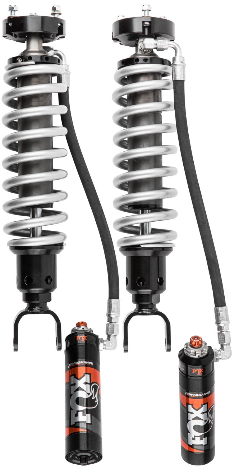 The image displays the Fox 19+ Ram 1500 2.5 Perf. Series Front Adjustable Coilover Shocks by FOX, designed for a 6-inch lift and featuring remote reservoirs. These performance shocks offer enhanced wheel travel and adjustability, with metallic coils connected to black shock absorbers, each attached to an individual cylinder reservoir through hoses.