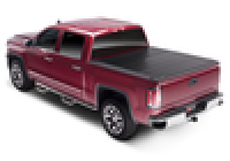 A red pickup truck featuring a sleek black BAKFlip FiberMax FRP surface tonneau cover by BAK over the bed, viewed from the rear and slightly to the side, showcases its advanced slam latch system for secure closure.