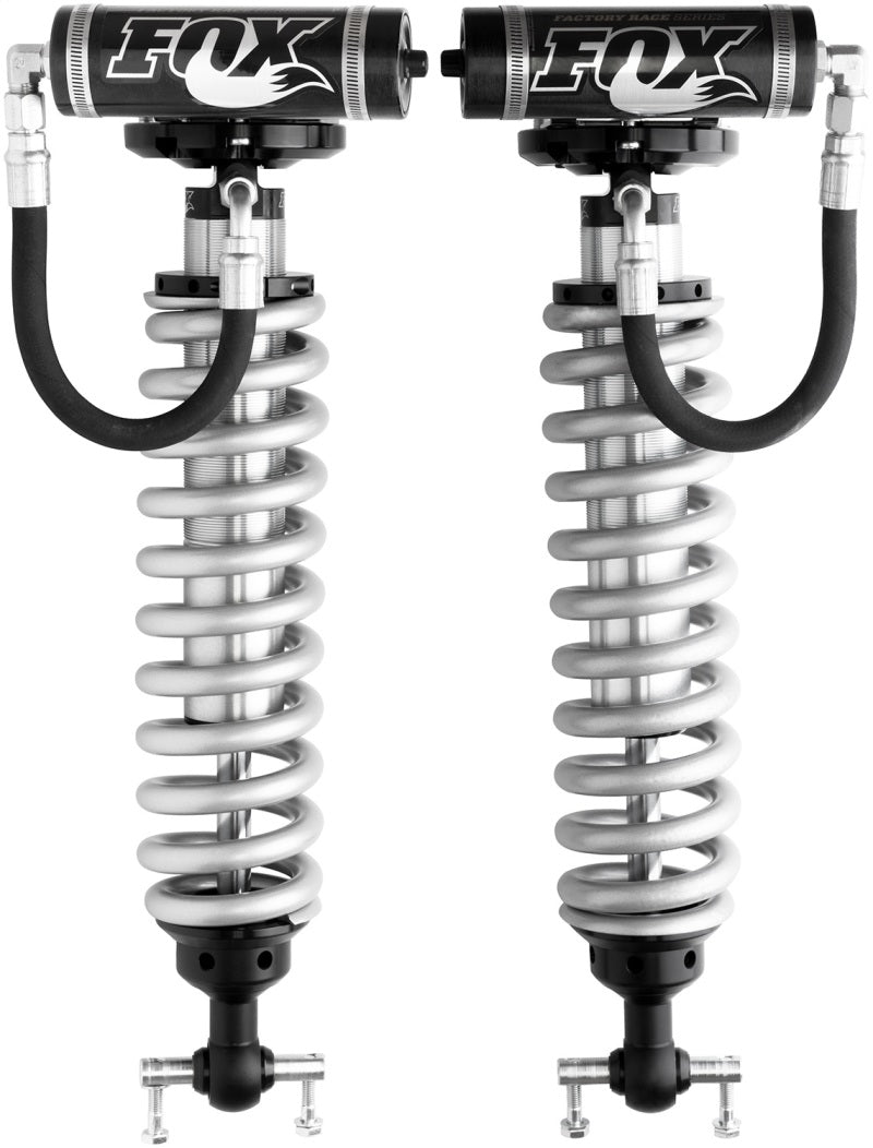 The Fox 2007+ Chevy 1500 Front 2.5 Factory Series Coilover Set for a 4-6.5 inch lift includes two silver shocks with black reservoirs and hoses, emblazoned with the "FOX" logo. These coilovers feature internal bypass technology, ideal for high-performance suspension systems to enhance off-road vehicle handling and comfort.