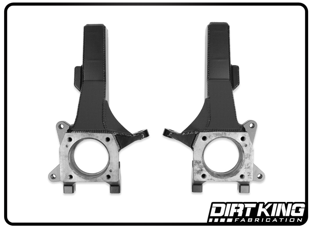 A pair of precision machined black metal automotive components designed for off-road performance in vehicle suspension systems. These symmetrical parts, manufactured by DIRT KING and labeled as the "05-23 Toyota Tacoma 6 Lug Performance Spindles," feature circular holes and metallic brackets.