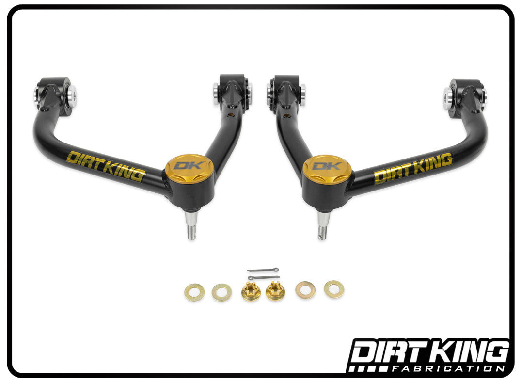 A set of black and gold 19-24 GM 1500 Ball Joint Upper Control Arms by DIRT KING, incorporating Moog ball joints and bushings, highlighted by a small metal pin, is expertly showcased against a white background. The DIRT KING logo graces the bottom right corner, underscoring superior suspension geometry.