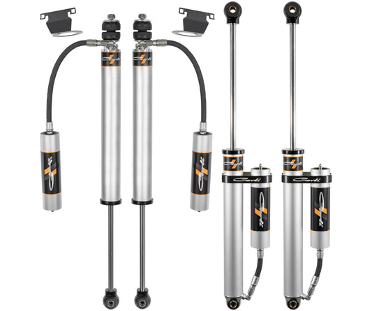 This image features the 13-23 Ram 3500 (4WD - Leaf) DIESEL Backcountry Leveling Shock Set by Carli Suspension, consisting of four silver shock absorbers with connected external reservoirs and black mounting brackets. They boast bold branding with striking orange accents, making them an essential component of a Suspension Lift Kit for a Ram 3500.