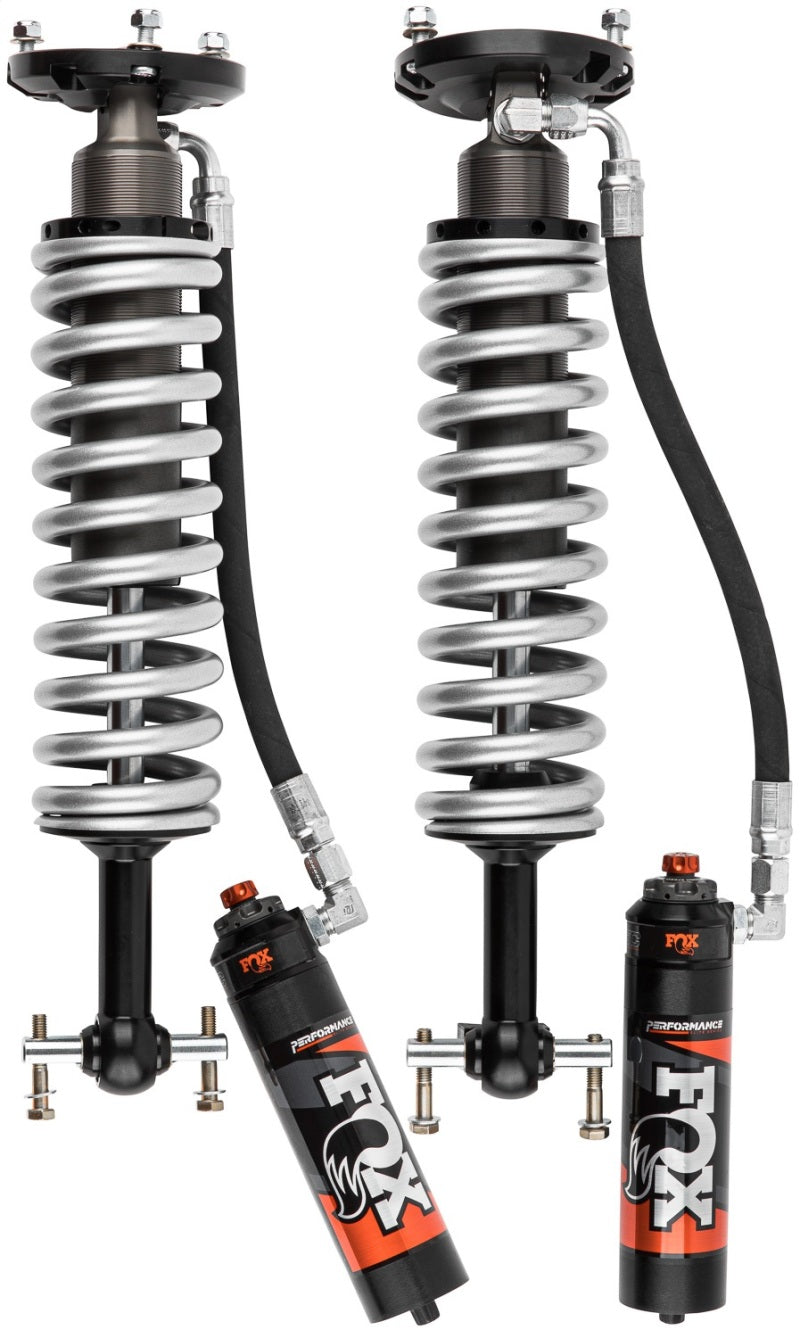 The Fox 19+ GM 1500 Non-TrailBoss/Non-AT4 0-2in Lift / TB/AT4 0in Lift 2.5 Series Front RR Coil Over shocks, featuring a black and silver design with external reservoirs, provide adjustability for increased wheel travel. Each shock is equipped with a coiled spring and an anodized finish, displaying the FOX logo in white and orange on the reservoir, making them excellent performance enhancements for high-performance vehicles.