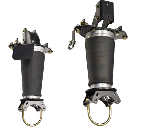 Two black air suspension struts, with metal brackets and fittings, are set against a white background. Designed for the Carli Suspension 19-23 Ram 3500 (4WD) Long Travel Air Bag System, these struts have slightly different sizes, with the left one being smaller than the right. Both feature U-shaped metal components at their base.