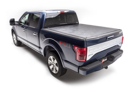 A blue pickup truck with a crew cab and covered truck bed is parked on a white background. It showcases silver accents, an "FX4" decal on the side, and is equipped with the BAK Revolver X2 hard aluminum roll-up cover for enhanced security, featuring automatic rotational locking rails.