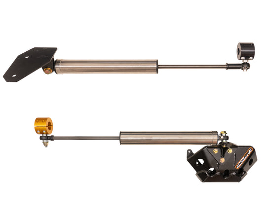 The 03-08 Dodge RAM 2500/3500 (4WD) Opposing Y-style Stainless Steel Stabilizer Kit from Carli Suspension is displayed, featuring two stabilizers with mounting brackets. The top stabilizer presents a straight cylindrical design, while the bottom one includes an angled bracket. Both employ a rod extending from the cylinder to provide improved control and performance.