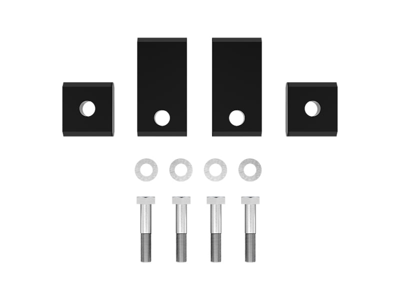 An arranged set of hardware components from the ICON 22+ Toyota Tundra Sway Bar Drop Kit features CNC machined aluminum pieces and parts including two large black metal brackets with holes, two smaller black square blocks with holes, four silver washers, and four silver bolts. These elements are displayed on a plain white background.