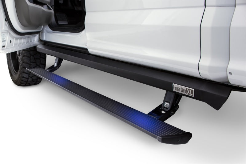 A white vehicle with its door open reveals an AMP Research Black PowerStep XL, an automatic electric-powered running board specifically designed for the 2017 Ford F-250/350/450 SuperCrew. The running board features blue lighting underneath, enhancing ease of entry for lifted trucks.