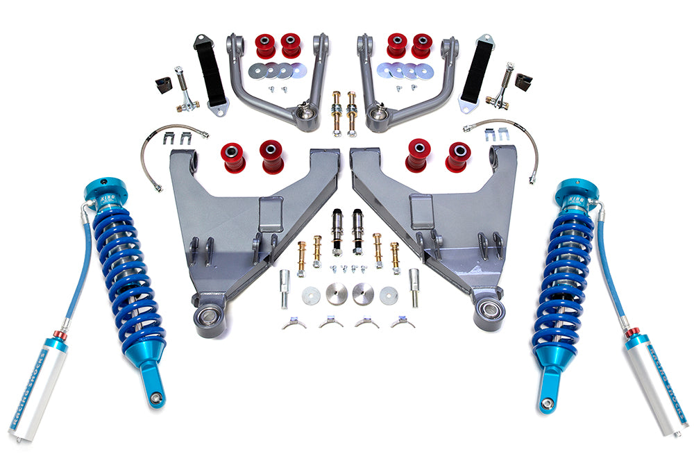 The 16-22 Toyota Tacoma +2 Inch Expedition Series Long Travel Kit with King Coil Overs from TOTAL CHAOS is displayed neatly. The kit includes blue coil-over shocks with reservoirs, large metal extended control arms, red urethane bushings, various bolts, nuts, washers, and small brackets organized symmetrically on a white background.