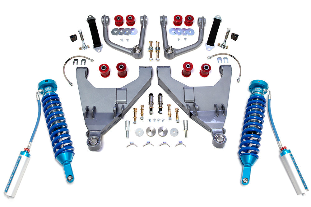 Image of a TOTAL CHAOS 05-15 Toyota Tacoma +2 Inch Expedition Series Long Travel Kit with King Coil Overs, showcasing multiple components laid out symmetrically. The kit includes blue King coil-over shocks with attached reservoirs, extended control arms, uniball components, red bushings, brake lines, nuts, bolts, washers, and other essential hardware—all meticulously arranged on a white surface.