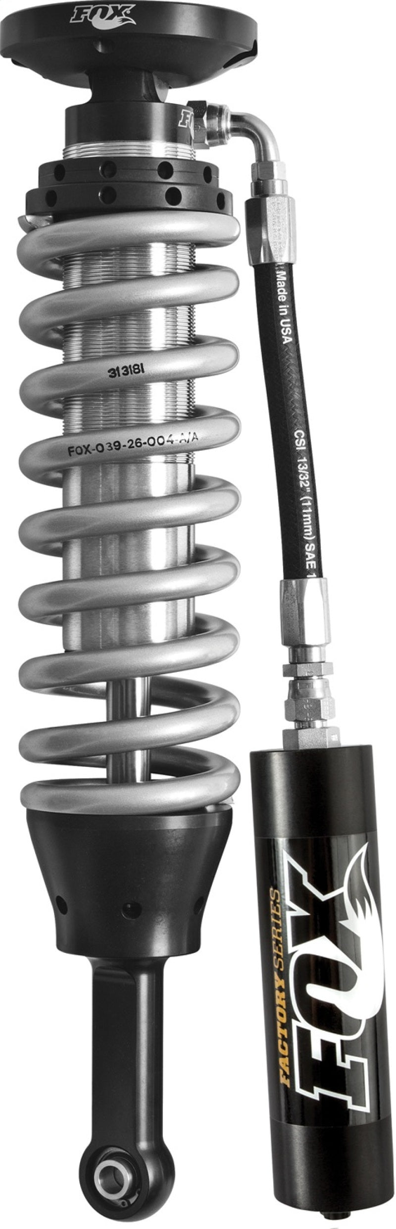 Close-up of a FOX shock absorber from the Fox 07+ Tundra 2.5 Factory Series, featuring a zinc-coated coil spring and an aluminum body with a reservoir. The metallic coil wraps around the cylinder, connecting to a black component. A flexible hose links the reservoir to the main assembly, displaying FOX branding and technical specifications, including Dual Speed Compression technology.