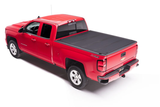 Viewed from above and behind, this red pickup truck with an aluminum matte finish showcases a sleek design. It’s a four-door Chevrolet Silverado outfitted with the BAKFlip MX4 heavy-duty truck bed cover by BAK, designed for the 14-18 Chevy Silverado 1500 and 15-20 Silverado 2500/3500 models with a 5ft 8in bed. The black, retractable cover accentuates its robust appearance while the tailgate prominently displays the logo.