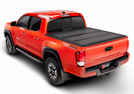 A vibrant orange pickup truck, featuring the BAKFlip MX4 Matte Finish truck bed cover from BAK, showcases TRD Off-Road and 4x4 decals. Photographed from a high rear angle, it highlights the strong construction and impressive off-road prowess.