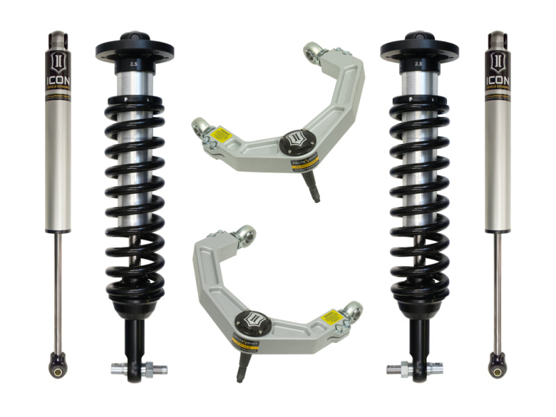 The image displays the ICON 2014 Ford F-150 2WD 0-2.63in Stage 2 Suspension System with Billet UCA, featuring a pair of shock absorbers with coil springs and two silver upper control arms. Highlighting the advanced Delta Joint for improved performance and corrosion resistance, the components are symmetrically arranged against a white background.