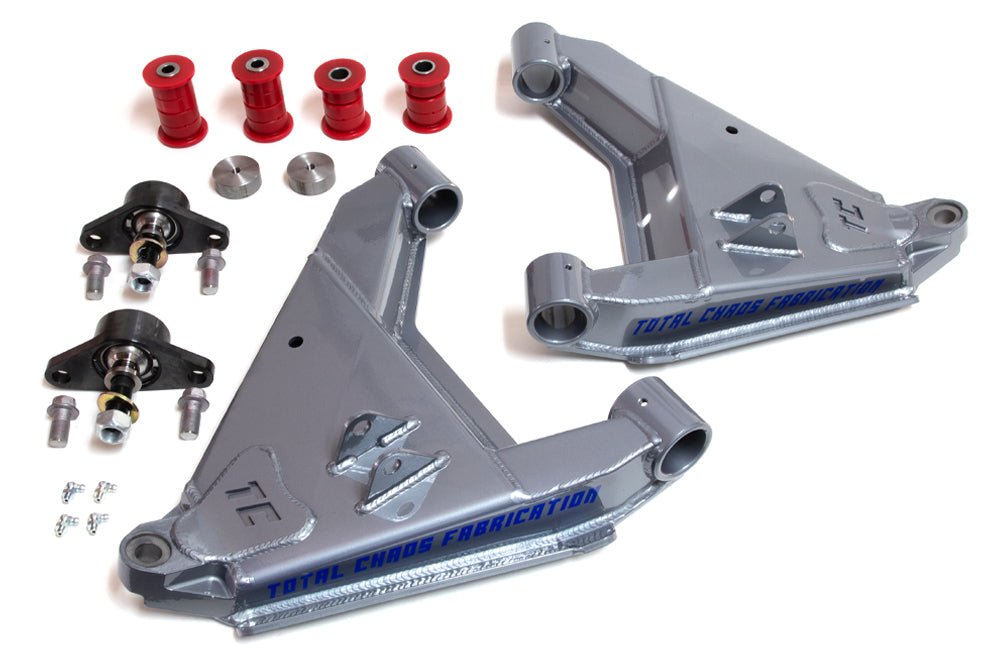 The image displays a set of TOTAL CHAOS 10-17 Toyota FJ Cruiser Standard Series Lower Control Arms, featuring two silver powder-coated control arms adorned with the "TOTAL CHAOS" logo, four red bushings, stainless steel uniballs, two ball joints, and an assortment of bolts and small parts meticulously arranged.