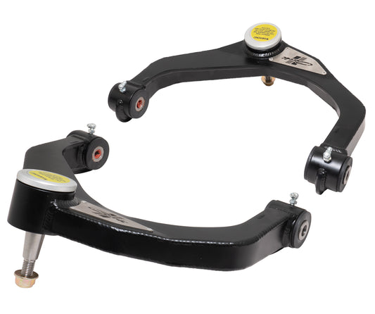 A pair of Carli Suspension Fabricated Upper Control Arms for the 09-22 Dodge Ram 1500 (4WD - Coil/Coil), featuring black coating with metallic accents and yellow labels, is crafted to enhance vehicle alignment and handling. These control arms, equipped with bushings and ball joints, are displayed facing each other against a white background.