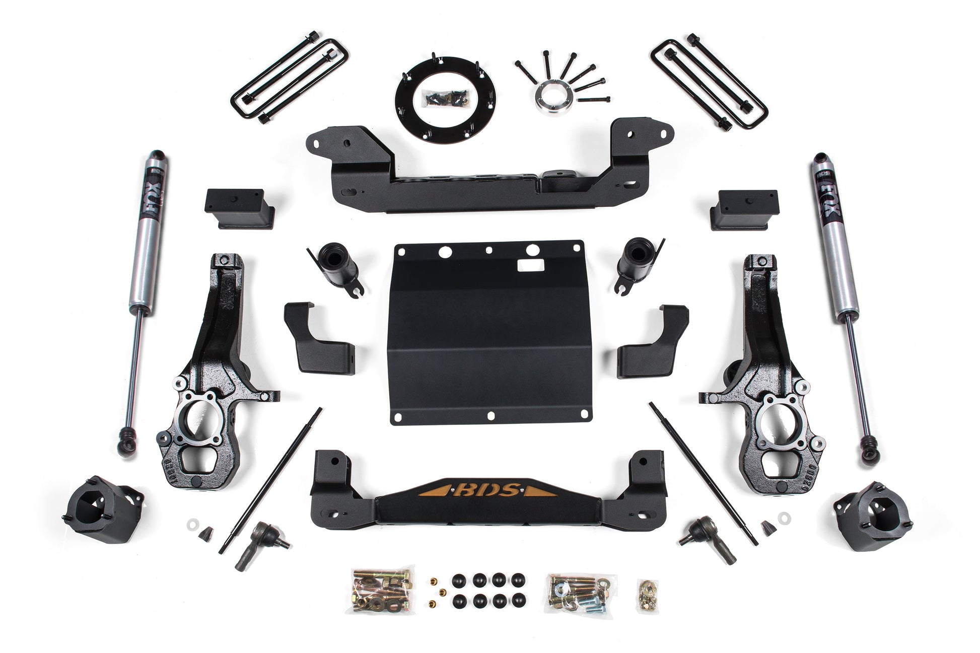 A variety of vehicle suspension components and hardware are neatly arranged in a flat lay. Visible parts include shock absorbers, mounting brackets, bolts, nuts, spacers, a skid plate for offroad protection, and other metal pieces—all designed for the BDS 5.5 Inch Lift Kit for the Chevy Colorado or GMC Canyon (2015-2022) 4WD.