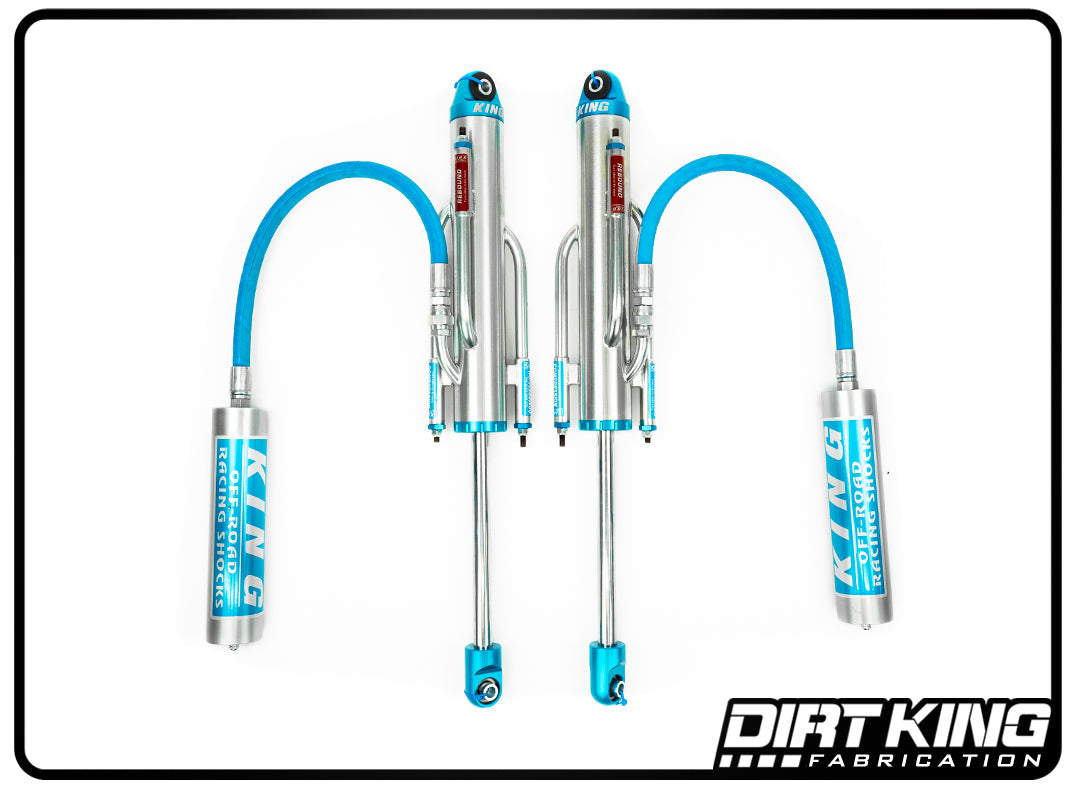 A pair of silver and blue shock absorbers with attached reservoirs, labeled "KING SHOCK TECHNOLOGY," are shown against a white background. These high-performance bypass shocks, part of the Dirt King 99-18 GM 1500 Long Travel Race Kit Spec King Triple Bypasses, provide superior suspension dampening. The "DIRT KING SHOCKS" logo appears in the bottom-right corner in bold white and black text.