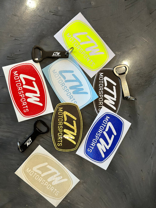 Introducing the LTW SWAG PACK from LTW Motorsports, a lively collection showcasing vibrant stickers in colors such as red, yellow, white, gold, blue, and black. Accompanied by two stylish bottle openers—one in red and one in black—this set is elegantly displayed on a dark surface.