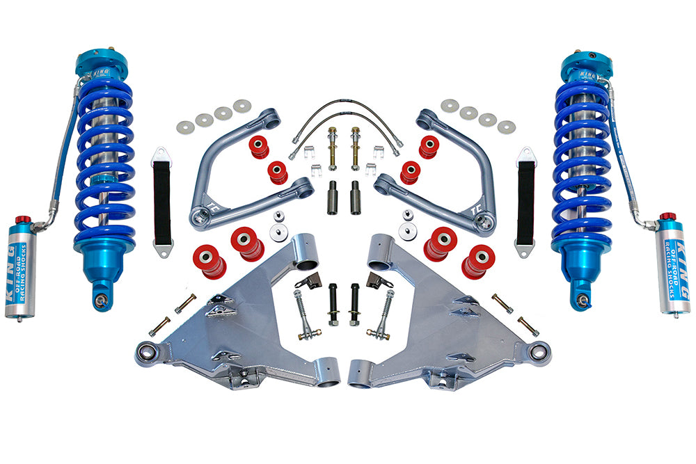 An array of off-road vehicle suspension components from the TOTAL CHAOS 07-21 Toyota Tundra +2.5 Inch Long Travel Kit with King Coil Overs, featuring two prominent blue King coilover shocks, silver Chromoly control arms, red and silver bushings, bolts, and other hardware designed to enhance wheel travel, symmetrically arranged against a white background.