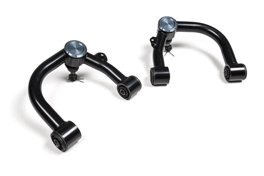 The image displays the BDS Upper Control Arm Kit for Toyota Tacoma (05-23), showcasing a pair of black automotive control arms with blue spherical joints. Constructed with high-strength tubular construction, these control arms are set against a plain white background. They feature bushings on one end and ball joints on the other, making them ideal for Toyota Tacoma UCA and fully compatible with BDS lift kits.