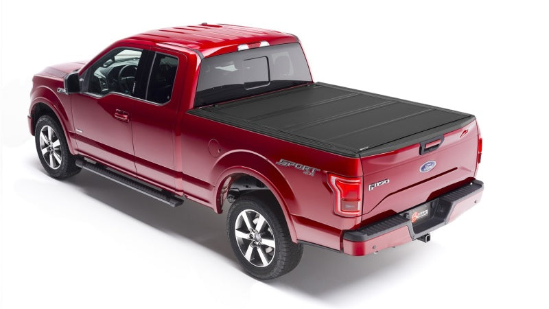 A red Ford F-150 pickup truck is equipped with a stylish black BAKFlip MX4 tonneau cover, featuring heavy-duty aluminum construction over its bed. "Sport" and "4x4" decals enhance its side and tailgate, beautifully highlighted in a well-lit setting against a white background.