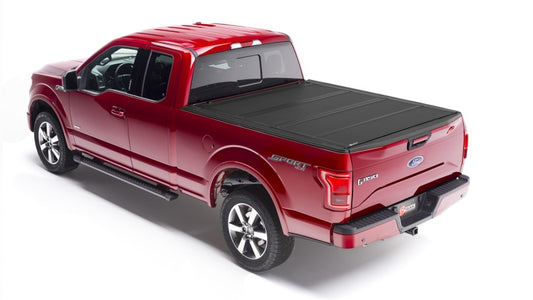 A red Ford F-150 pickup truck is equipped with a stylish black BAKFlip MX4 tonneau cover, featuring heavy-duty aluminum construction over its bed. "Sport" and "4x4" decals enhance its side and tailgate, beautifully highlighted in a well-lit setting against a white background.