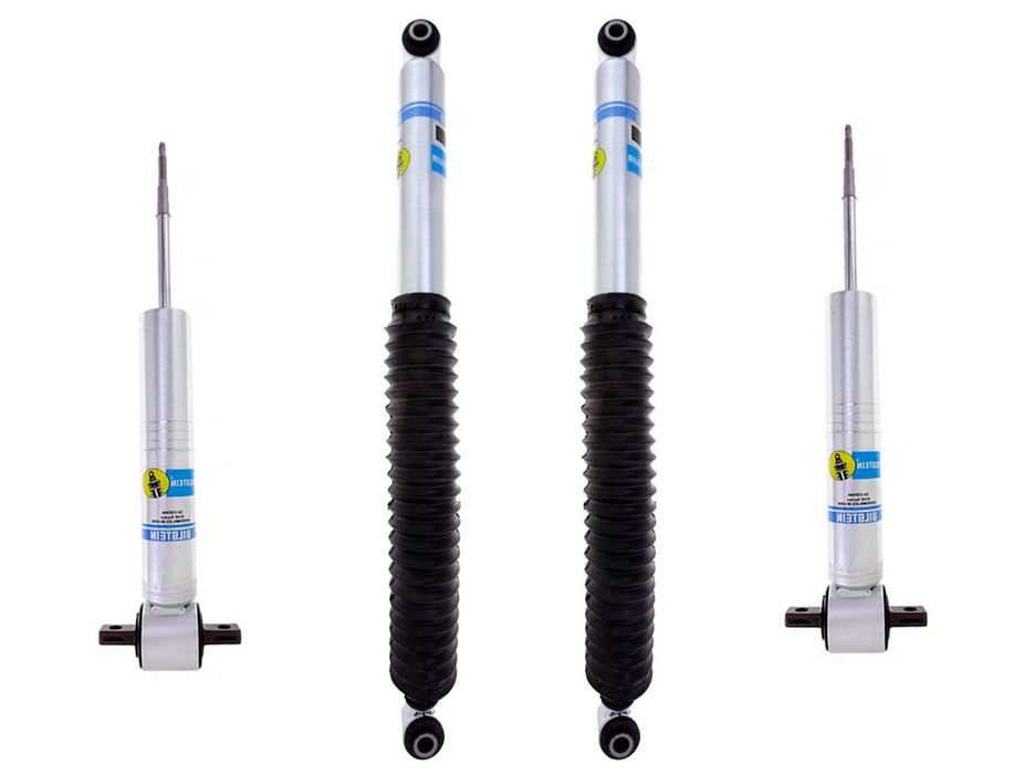 The LTW Motorsports 19-24 GM 1500 AT4/Trail Boss Leveling Kit with Bilstein 5100 Shocks includes four vehicle shock absorbers, two in a compressed state and two in an extended state. They are predominantly silver with blue and yellow labels, making them ideal for off-road performance. The extended length struts feature black corrugated dust covers, perfect for enhancing your Bilstein Leveling Kit.