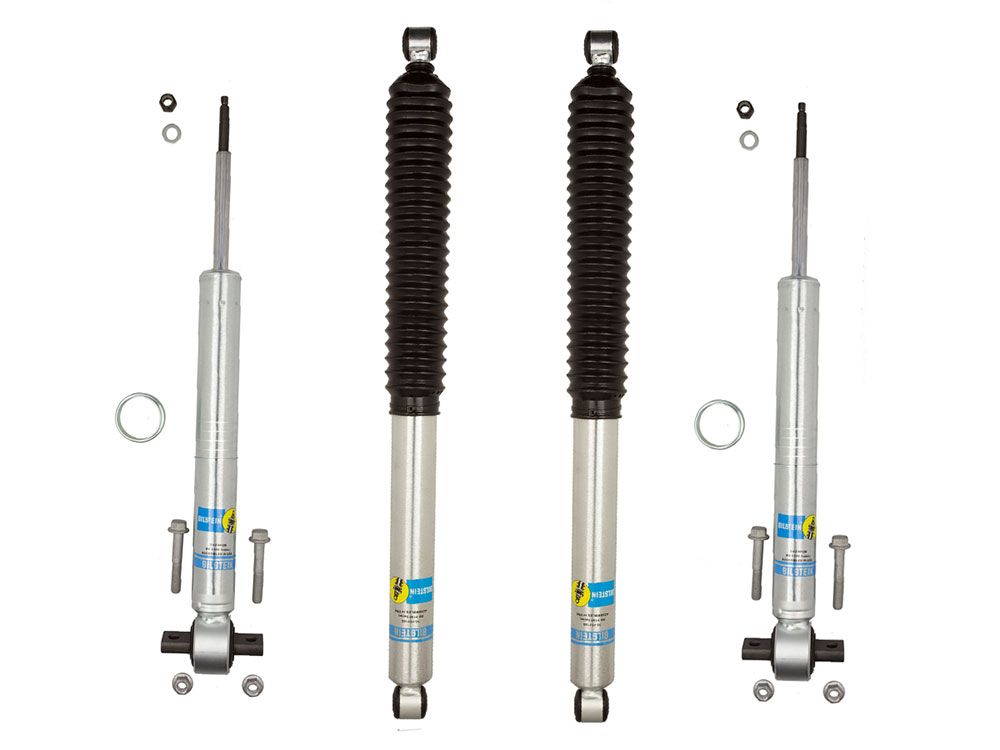 The LTW Motorsports 21-23 Ford F-150 Leveling Kit with Bilstein 5100 Shocks includes four silver shock absorbers adorned with blue and yellow logos. Two of these shocks have black protective sleeves. The kit also comes with small metal rings and bolts, all presented against a white background.