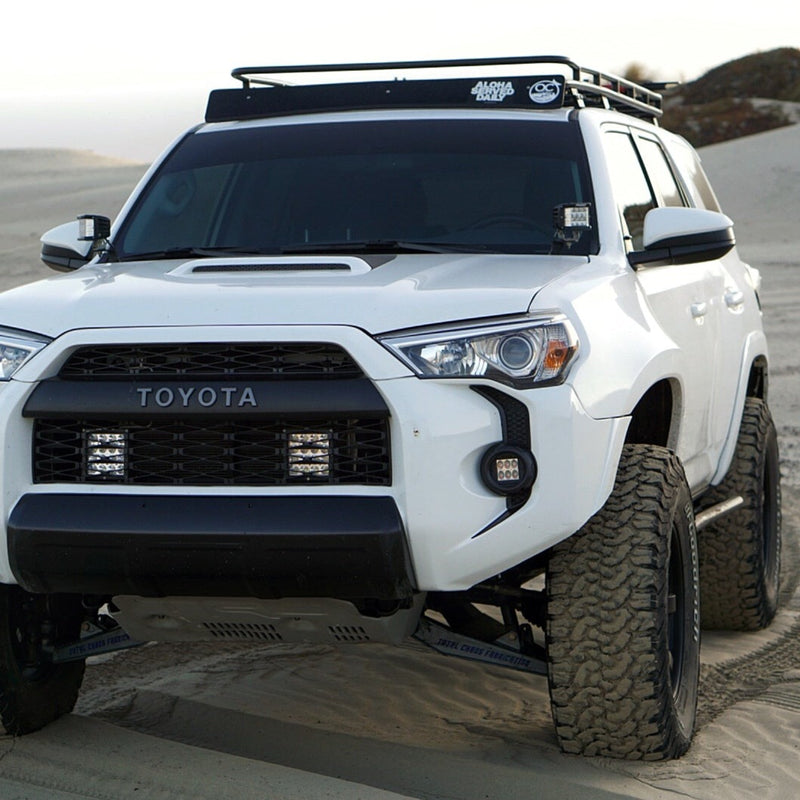 A white Toyota 4Runner SUV, outfitted with ADV Fiberglass 2010-2023 Toyota 4-Runner fenders, elevated suspension, large all-terrain tires, and additional front lighting, parked on a sandy desert terrain. The vehicle also features a roof rack and window stickers.