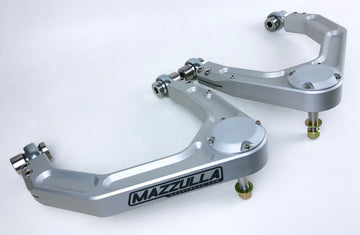 Two identical, silver-colored metal automotive parts with the brand name "MAZZULLA OFFROAD" clearly visible. Each component, identified as 2019+ CHEVY/GMC 1500 BILLET UPPER CONTROL ARMS, features a curved, arm-like structure with a central pivot point and mounting points at both ends. The parts are shown against a plain white background.