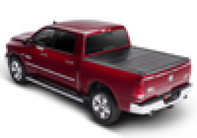 A red pickup truck with a BAK 02-18 Ram 1500 (19-20 Classic Only) / 03-20 Ram 2500/3500 6ft 4in Bed (w/o Ram Box) BAKFlip F1 black hard folding truck bed cover is viewed from the rear left side. The vehicle features tinted windows and chrome accents on the wheels and side step bars.