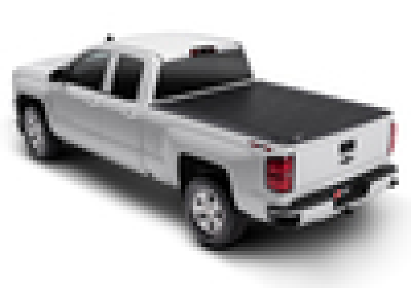 A white, four-door Chevy Silverado pickup truck viewed from the rear and slightly above features a BAK 04-13 Chevy Silverado 5ft 8in Bed Revolver X2 black, hard rolling truck bed cover. This aluminum roll-up cover seamlessly integrates into the truck's sleek, modern design. The tailgate is closed and the vehicle is showcased on a white background.