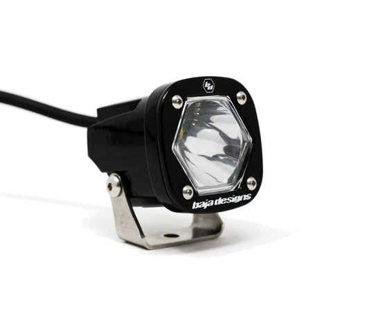 The Baja Designs S1 Spot LED Light w/ Mounting Bracket Single is a compact, black, hexagonal fixture with a transparent lens and a robust metal mounting bracket. The front displays the "Baja Designs" brand, and the light is seamlessly connected to an elegant black cable.