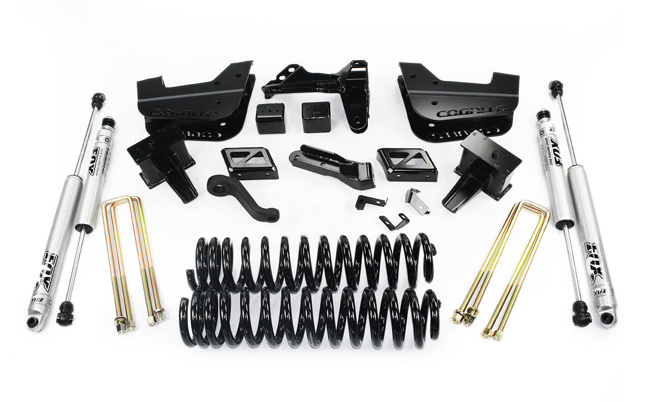 The Cognito 4-Inch Standard Lift Kit With Fox PS 2.0 IFP Shocks for 11-16 Ford F-250/F-350 4WD, displayed on a white background, includes two silver Fox 2.0 Performance Series shocks, several black coil springs, black metal brackets, gold U-bolts, and other Cognito Motorsports components. These parts are arranged neatly in rows.