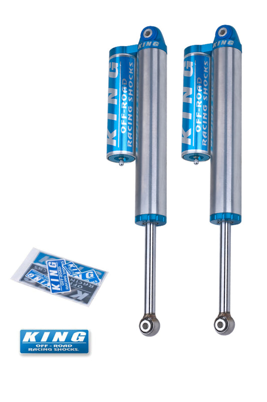 Two King Shocks 07-18 Chevrolet/GMC Silverado/Sierra 1500 Rear 2.5 Dia Piggyback Res Shocks, part of the bolt-on suspension system, are displayed in blue and silver against a white background. Below the shocks, a small packet contains stickers and a logo that reads "KING" in blue text.