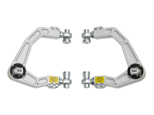 The image shows the ICON 2019+ Ford Ranger Billet Upper Control Arm Delta Joint Kit, a set of silver-colored adjustable upper control arms designed for a vehicle's suspension system. Each arm features two attachment points, warning labels, and an intricate geometric design with multiple cutouts to reduce weight. Additionally, they are equipped with Delta Joint heavy-duty high angle ball joints for superior performance.