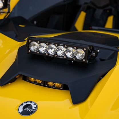 A close-up of a Can-Am Maverick reveals its distinctive yellow body adorned with a set of four LED lights mounted on the hood. Below the lights, the BRP logo is prominently displayed, highlighting the tough Baja Designs Can-Am Maverick R Clear 10in OnX6+ Shock Tower Kit engineered for exceptional off-road adventures.