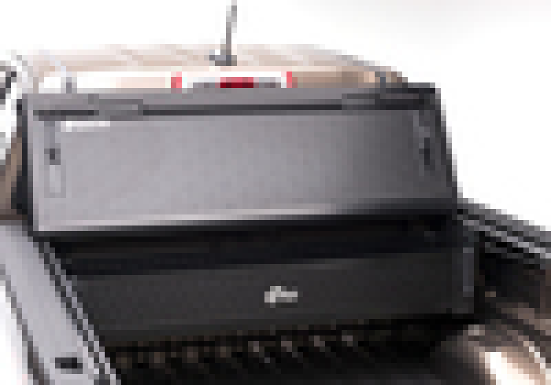 A pixelated image shows an item, possibly a piece of equipment or machinery, with a black and gray exterior. It is placed within a larger metallic structure, resembling the sleek design of the BAK 05-20 Nissan Frontier 6ft BAK BOX 2 toolbox from BAK. The specific details of the image are unclear due to the pixelation.