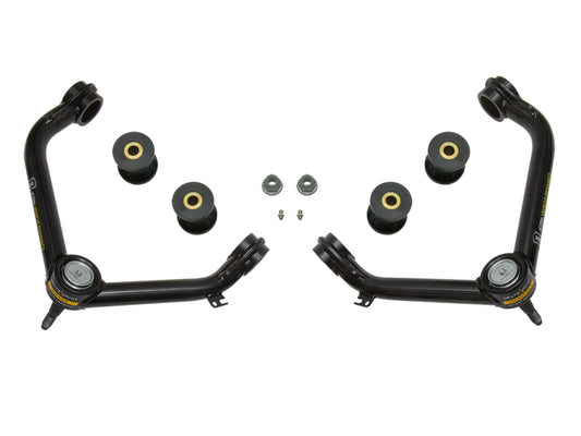 Image of the ICON 2009+ Ram 1500 Tubular Upper Control Arm Delta Joint Kit by ICON, showcasing a pair of black upper control arms with attached bushings and heavy-duty ball joints. The set includes four additional black cylindrical bushings with yellow centers, as well as two small bolts with nuts. The components are symmetrically arranged for display.