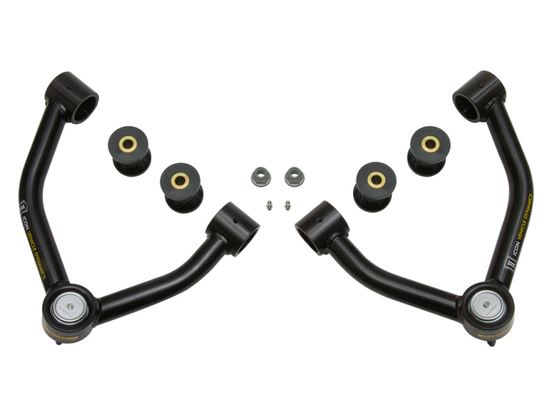 A pair of black, curved ICON 2015+ Chevrolet Colorado Tubular Upper Control Arm Delta Joint Kits is positioned symmetrically, with bushings and washers placed between them. These heavy-duty parts feature Delta Joints and have cylindrical openings on either end along with some visible ICON branding.