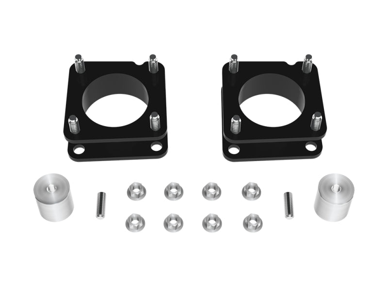 The ICON 2022+ Toyota Tundra 2.25in Front Spacer Kit by ICON features black metal components with circular cutouts and attached threaded rods, along with silver cylindrical spacers, screws, and nuts, all arranged neatly on a white background—perfect for a front coilover installation on your 2022 Toyota Tundra leveling kit.