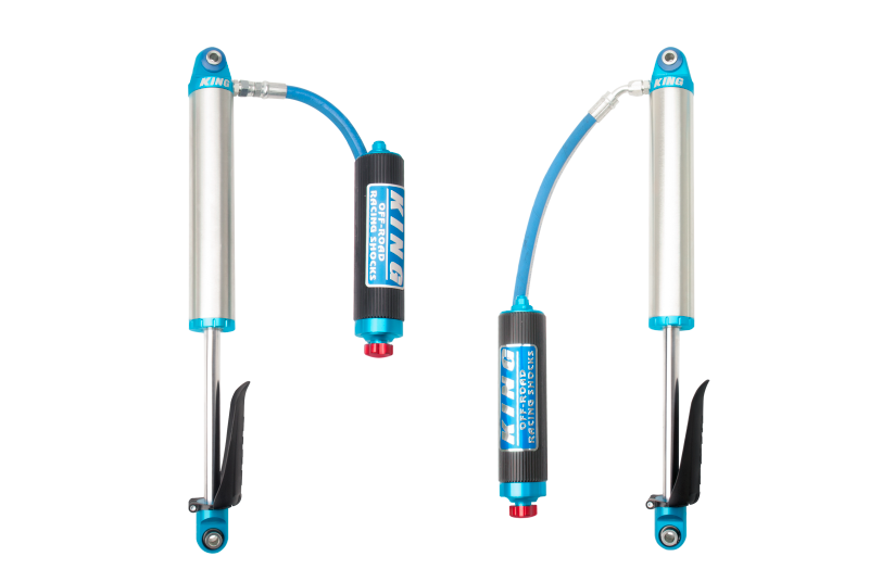 Two hydraulic shock absorbers with attached reservoirs, connected by a flexible tube. The shocks are silver, blue, and black, branded "KING OFF-ROAD RACING SHOCKS" in blue on the black reservoirs. The bottom mounts feature black protective sleeves and red adjustment knobs for custom valve adjustments. This is an ideal OEM performance upgrade kit specifically designed for the 2019+ Chevrolet Silverado 1500 (Trail Boss), known as the King Shocks Rear 2.5 Dia Remote Res Shock w/Adj (Pair).