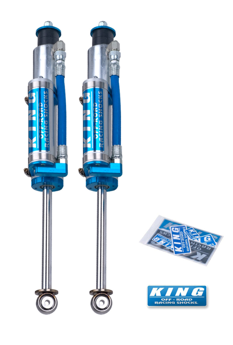 The image shows two blue and silver shock absorbers branded with "King Shocks." These shocks, specifically the King Shocks 2005+ Ford F-250/F-350 4WD Front 2.5 Dia Remote Reservoir Shock (Pair), are part of the OEM Performance Upgrade Kits and are placed side by side. Below them, there are King branded stickers and a lanyard. The shock absorbers feature external reservoirs connected via blue hoses.