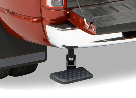 A close-up view of a red truck's rear end with an open tailgate features the AMP Research 2002-2008 Dodge Ram 1500 BedStep - Black. The extended black BedStep, designed by AMP Research, is attached beneath the tailgate to assist with climbing into the truck bed. It has a textured surface for traction and is aligned with the truck's bumper.