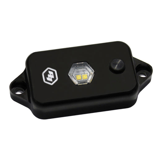 The small, rectangular black sensor device from Baja Designs, known as the LED Dome Light with Switch - Clear, features mounting holes on either side. It boasts a hexagonal clear window that reveals internal components and includes a round button on the surface.