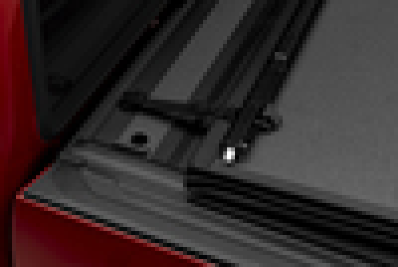 Close-up of the rear edge of a red Toyota Tundra pickup truck bed with a black BAKFlip MX4 Matte Finish hard-folding tonneau cover partially opened, revealing the hinge and latch mechanism. The heavy-duty aluminum BAK cover appears secure, well-fitted to the 5ft 6in bed with OE Track System, and boasts UV and scratch resistance.